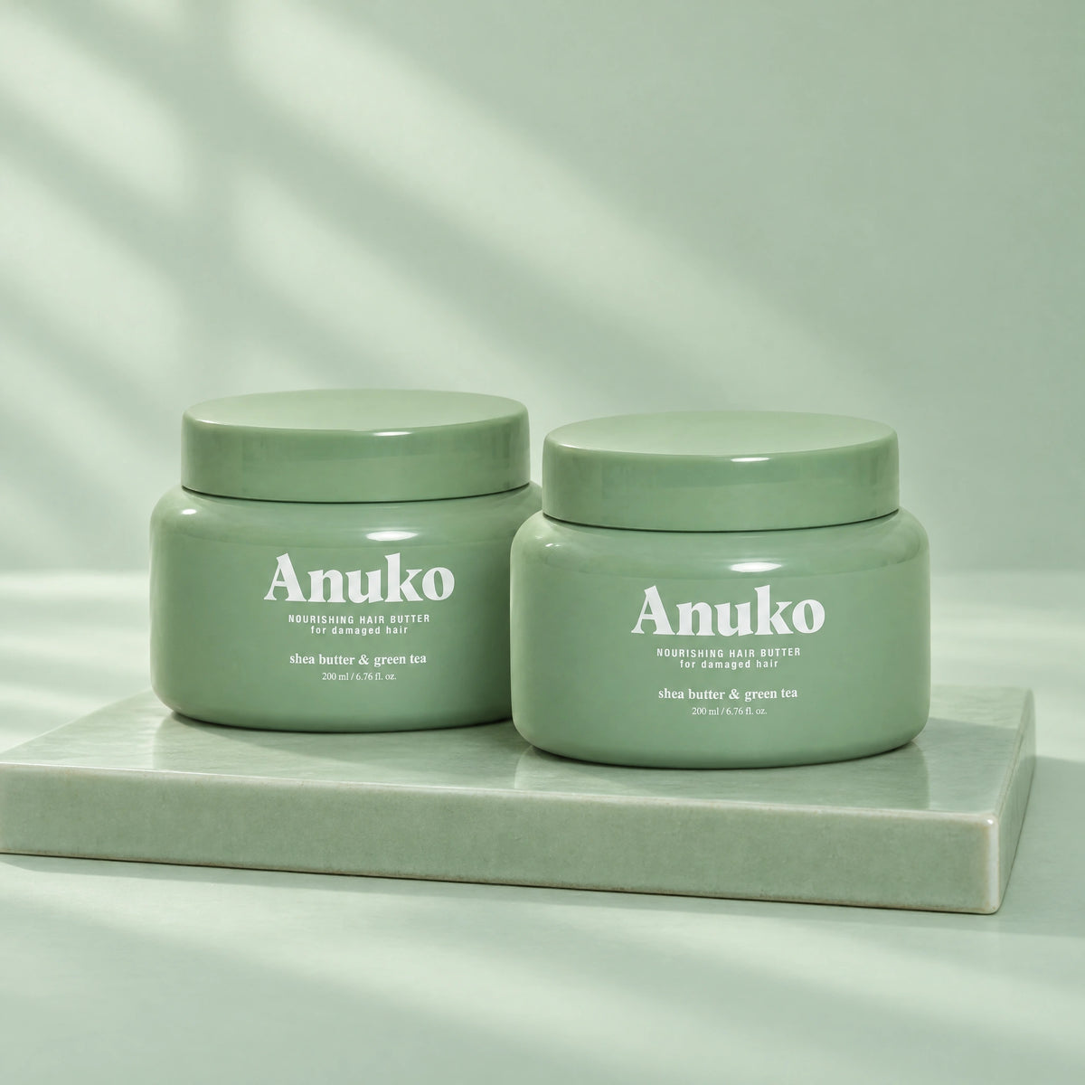 Two Anuko Nourishing Hair Butter jars on a celadon tile plinth