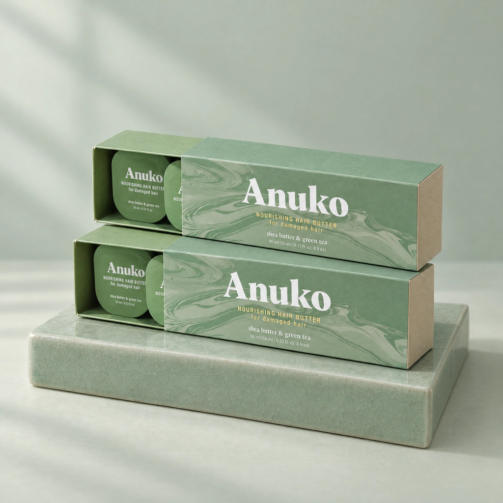 Two Anuko Travel Hair Butter cases stacked on a celadon tile plinth