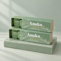 Two Anuko Travel Hair Butter cases stacked on a celadon tile plinth