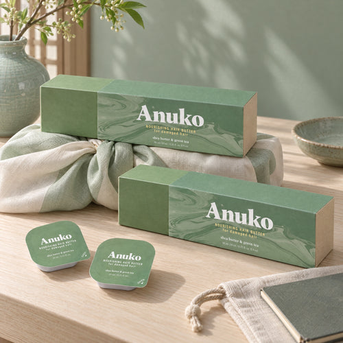 Two Travel Hair Butter cases, one on a knotted bojagi gift wrap, with capsules, a linen pouch and a notebook